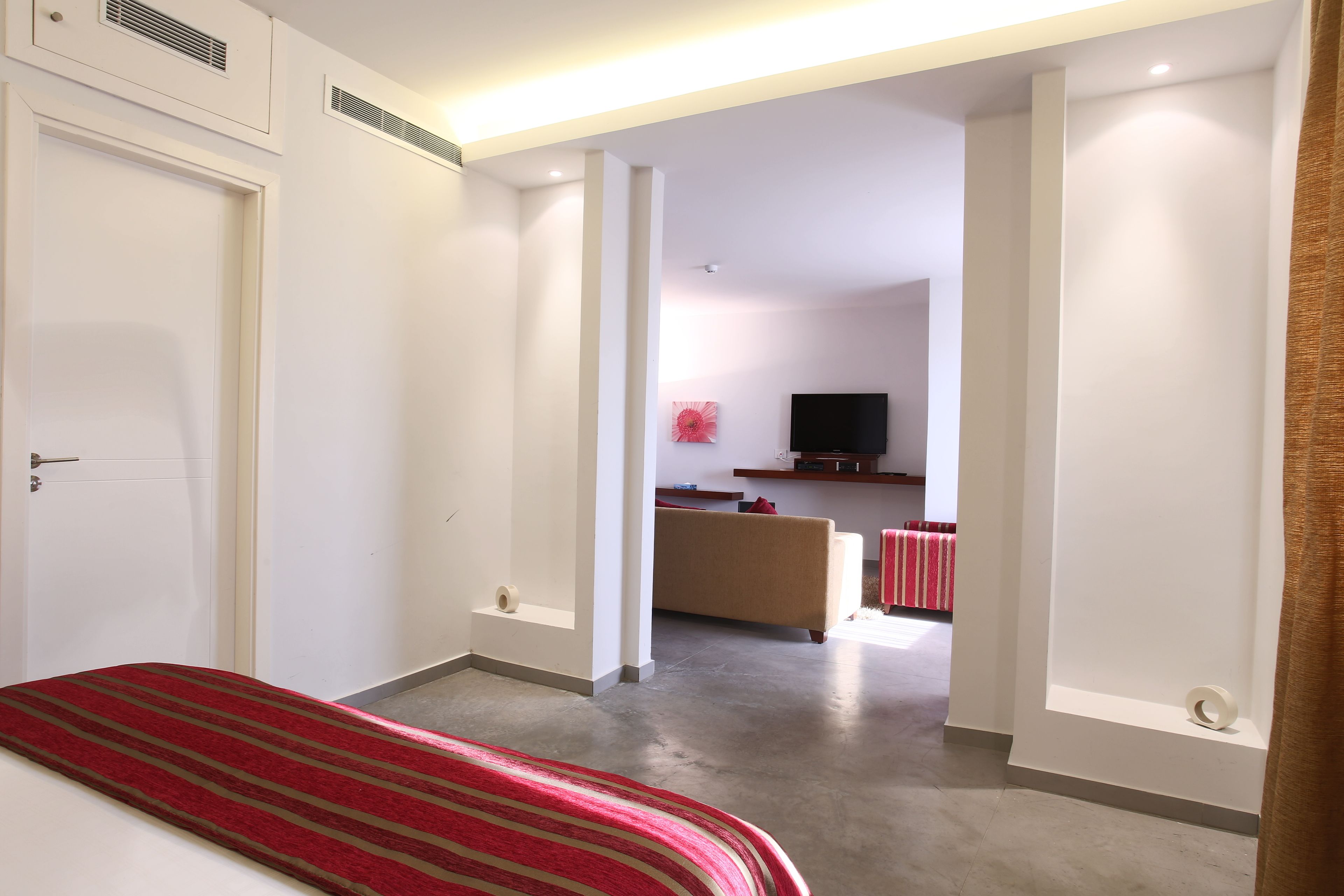 A hotel room with a bed, a TV, a sofa, and a red-striped rug.