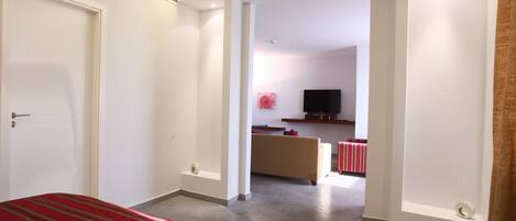 A hotel room with a bed, a TV, a sofa, and a red-striped rug.