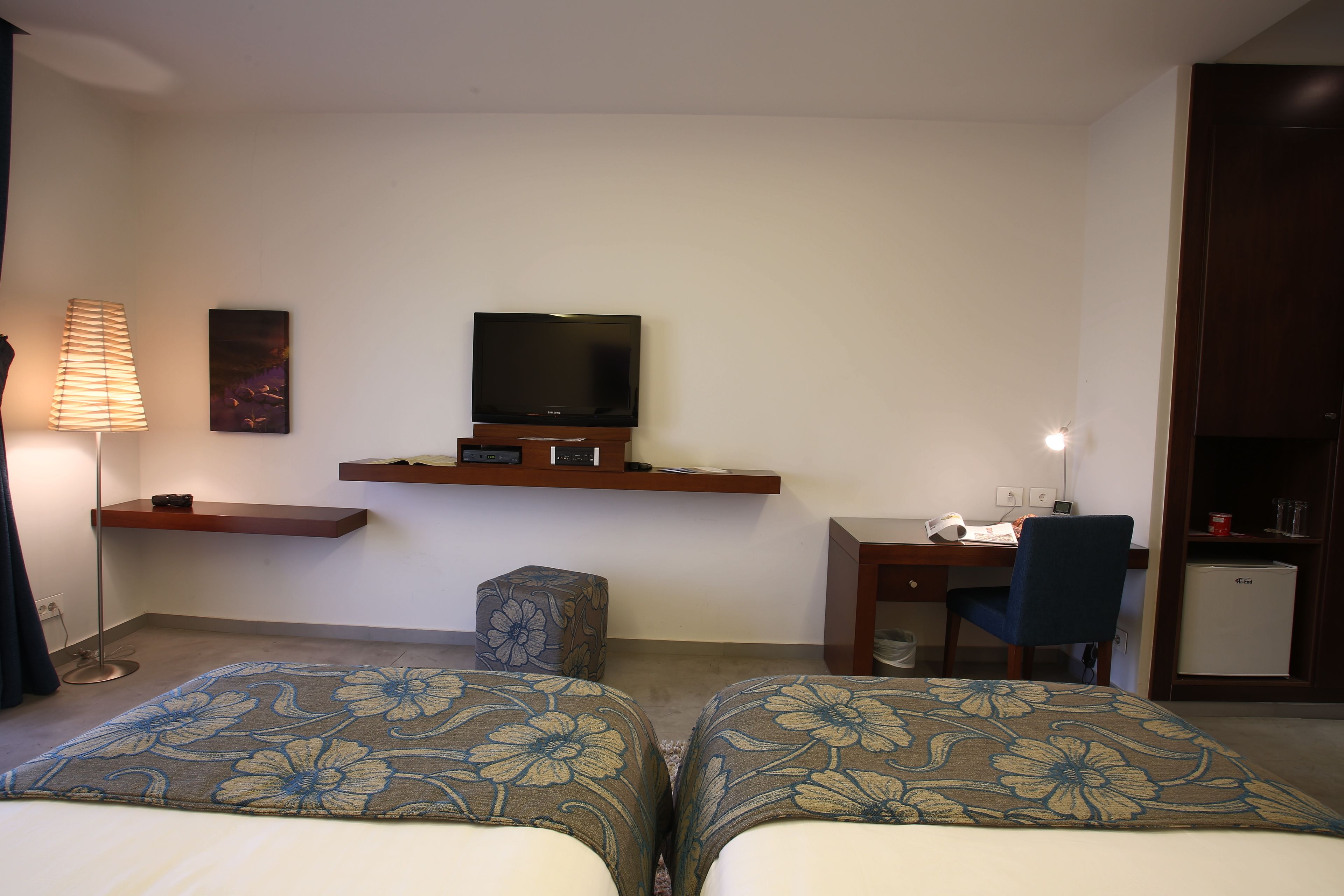 A hotel room with two beds, a desk, a television, a chair, and a small refrigerator.