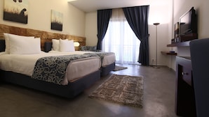A modern hotel room with two beds, a flat-screen TV, and a large window with curtains. - Monoberge Byblos Hotel (Byblos)