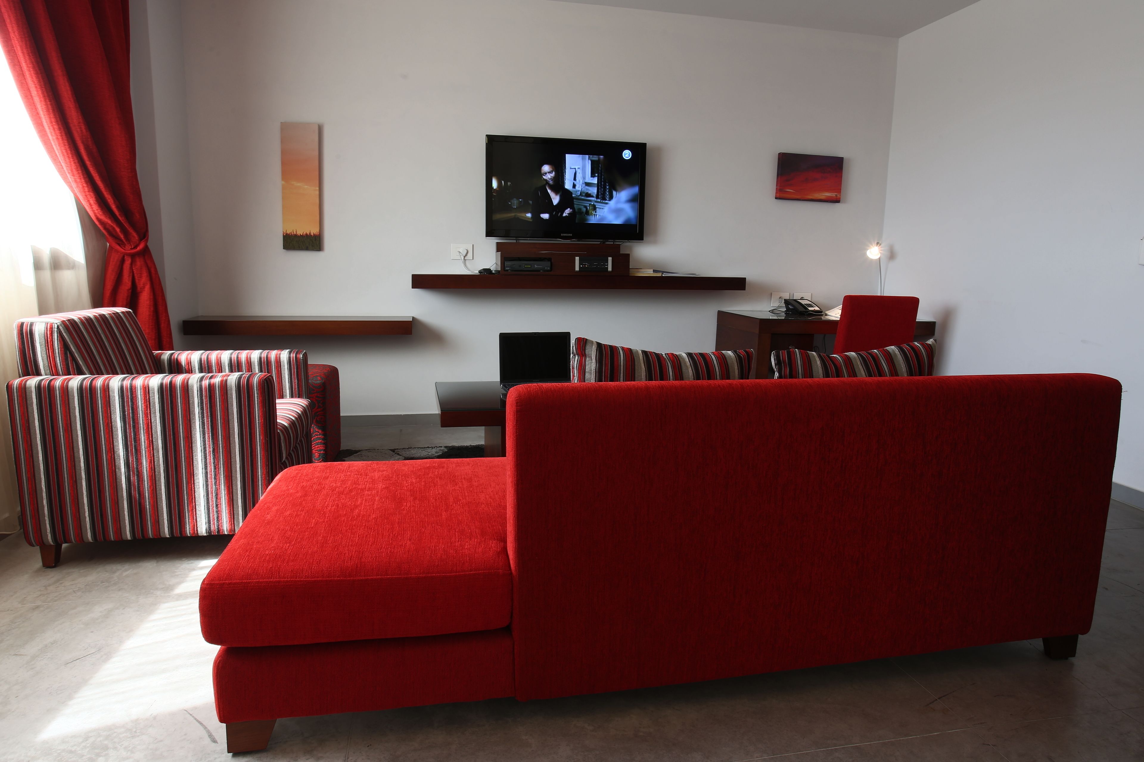 Uma sala de estar moderna com um sofá vermelho, poltronas listradas, uma TV de tela plana e uma mesa de centro de madeira.