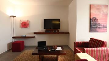 A modern living room with a flat-screen TV, a laptop, a red ottoman, a striped armchair, and a painting on the wall.
