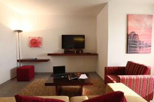 Una sala de estar moderna con un televisor de pantalla plana, una computadora portátil, un reposapiés rojo, un sillón a rayas y un cuadro en la pared.