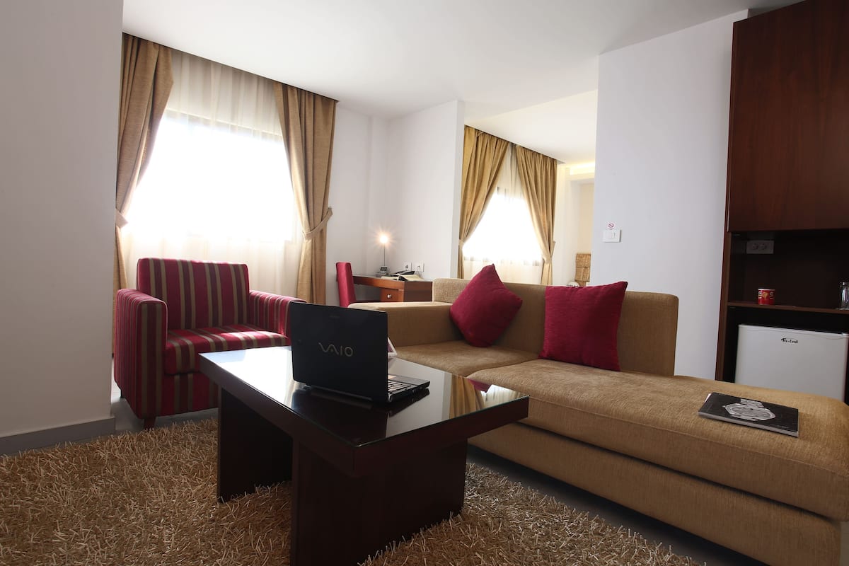 A modern living room with a sofa, a red armchair, a coffee table with a laptop, and a small refrigerator.