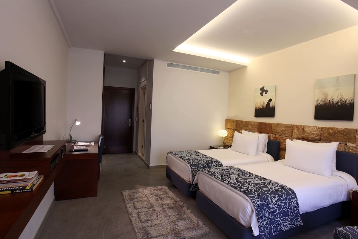 A hotel room with two beds, a desk with a TV, and artwork on the wall.