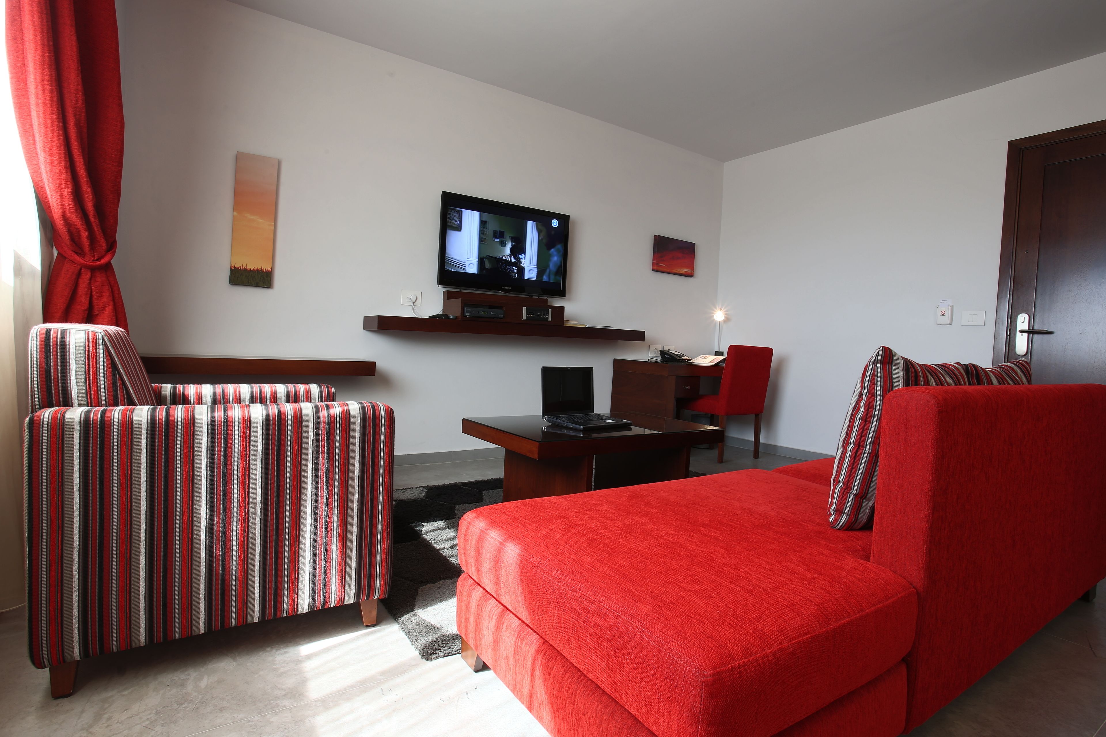 Una sala de estar con un sofá rojo, un sillón a rayas y un televisor sobre un mueble.