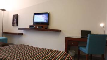 A hotel room with a bed, a desk, a chair, a television, and a trash bin.