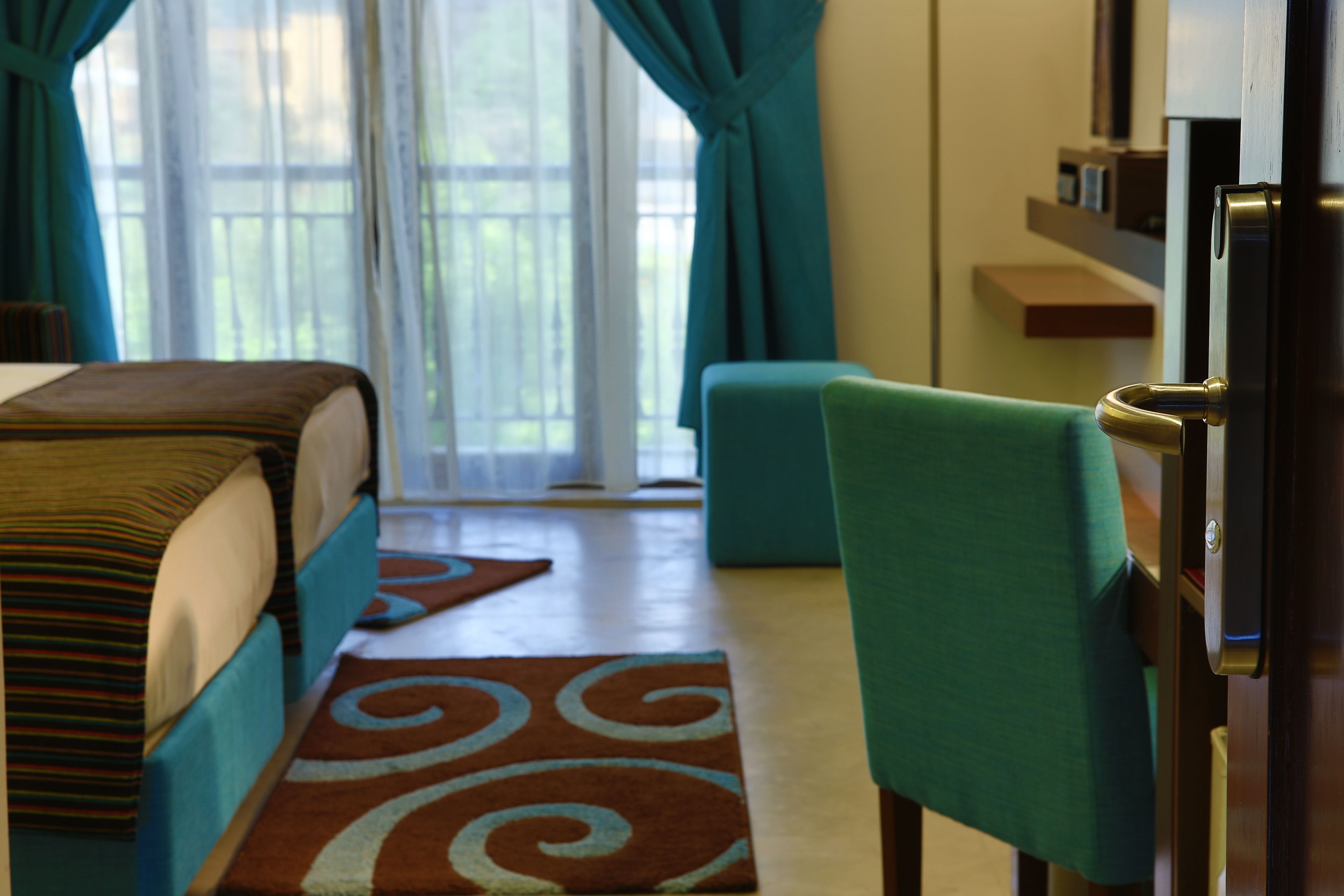 A hotel room with a bed, a green armchair, a TV, and a window with curtains.