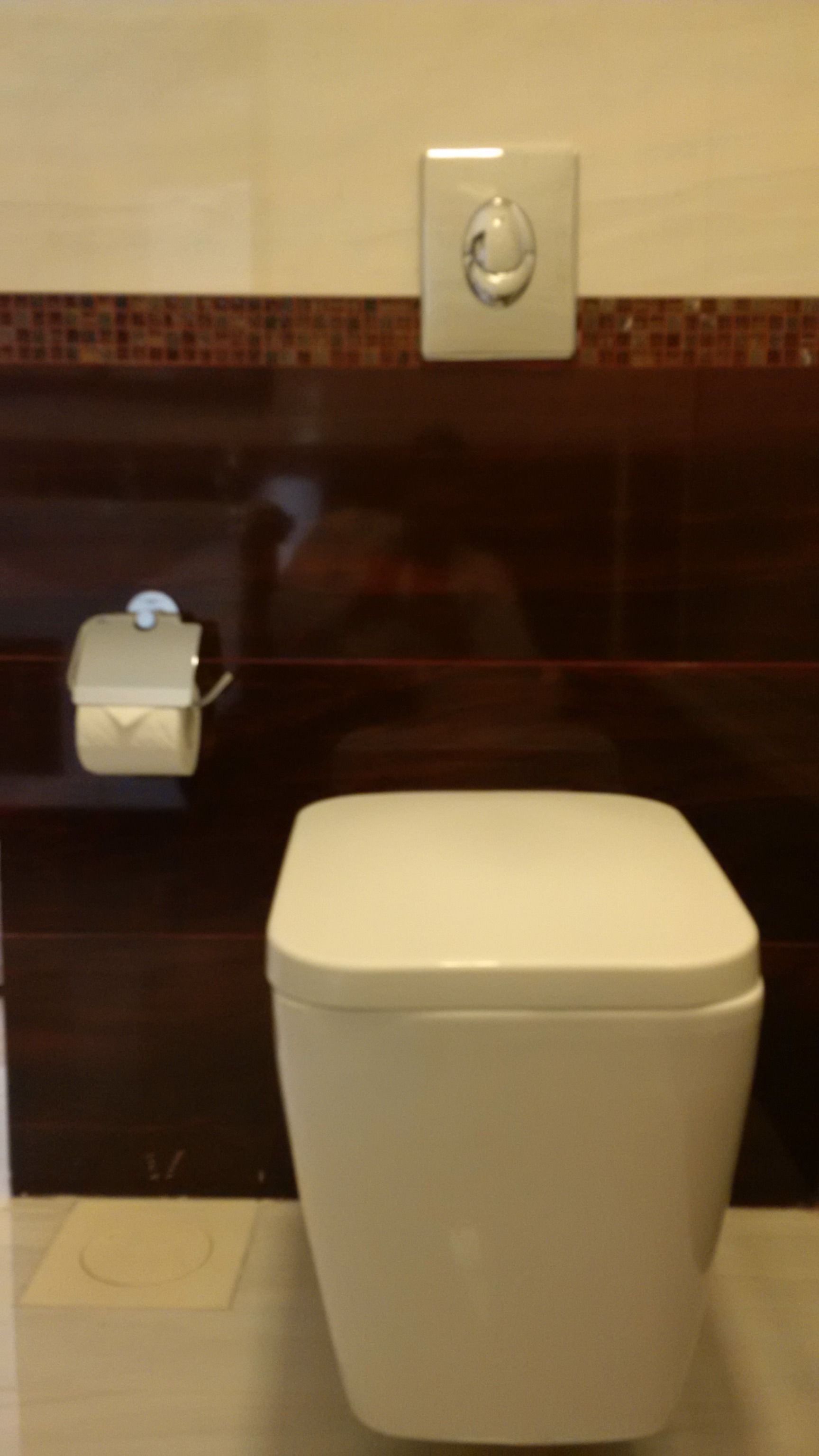 A toilet with a white lid, a hand dryer, and a paper towel dispenser.