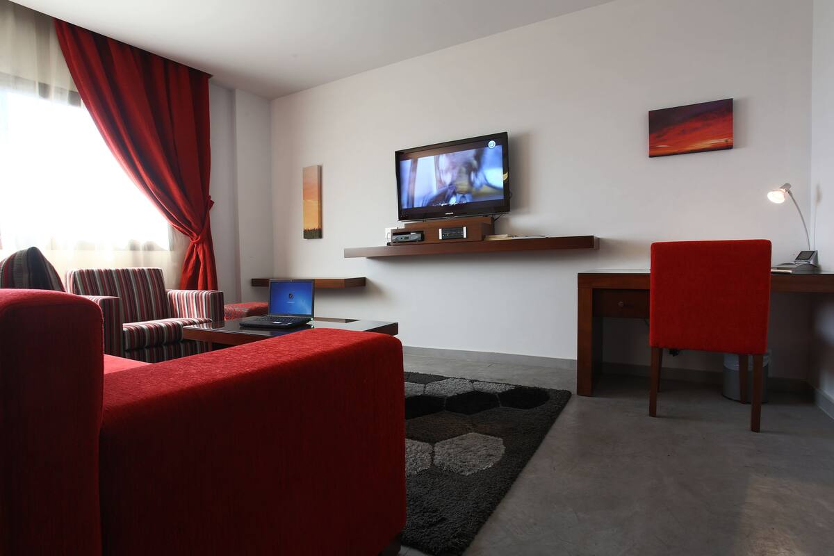 A modern living room with a flat-screen TV, a laptop, and a red chair.