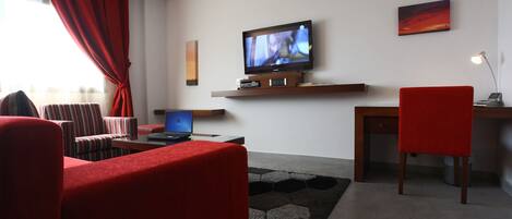 Una sala de estar moderna con un televisor de pantalla plana, una computadora portátil y una silla roja.