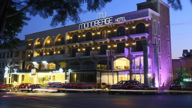 A hotel with multiple balconies, a prominent sign, and a parking area with cars. - Monoberge Byblos Hotel (Byblos)