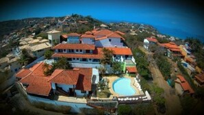 Vue aérienne d’un quartier résidentiel situé sur la côte, avec de nombreuses maisons, une piscine et une vue sur la mer.