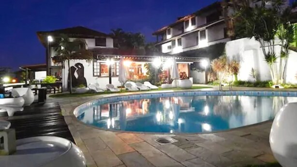 Une vue nocturne d’un hôtel avec une piscine, des chaises longues et un espace extérieur bien éclairé.
