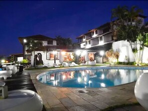 A nighttime view of a hotel with a swimming pool, lounge chairs, and a well-lit outdoor area. - Arambaré Buzios Hotel (Búzios)