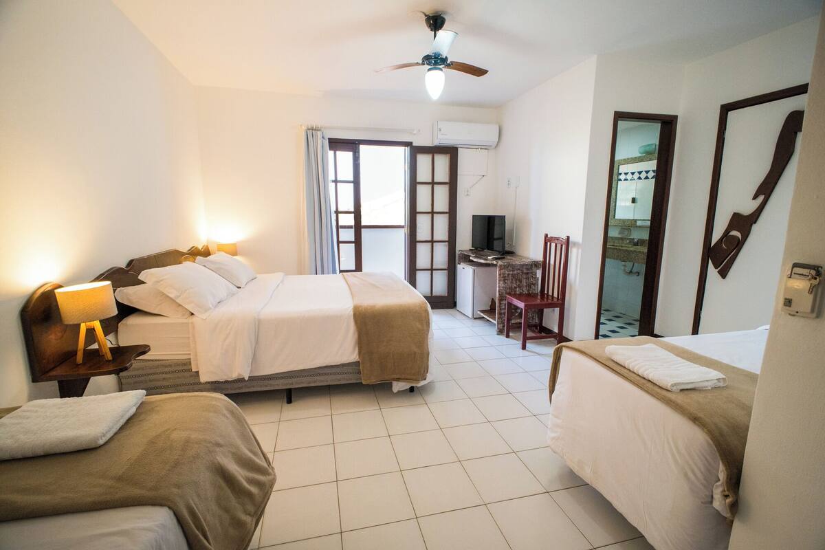 A hotel room with two beds, a desk, a chair, a ceiling fan, and an air conditioning unit.