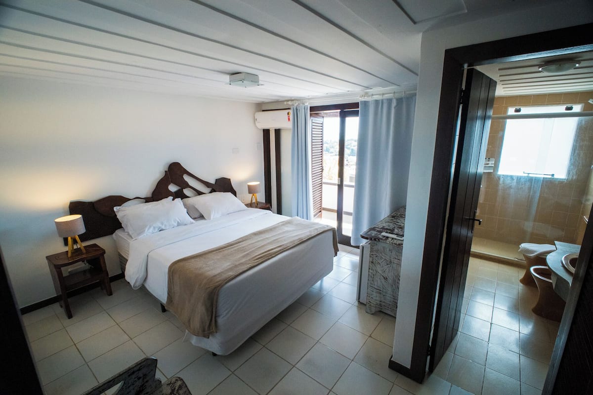 A hotel room with a bed, bedside tables, a lamp, a view of the outside, and a bathroom.