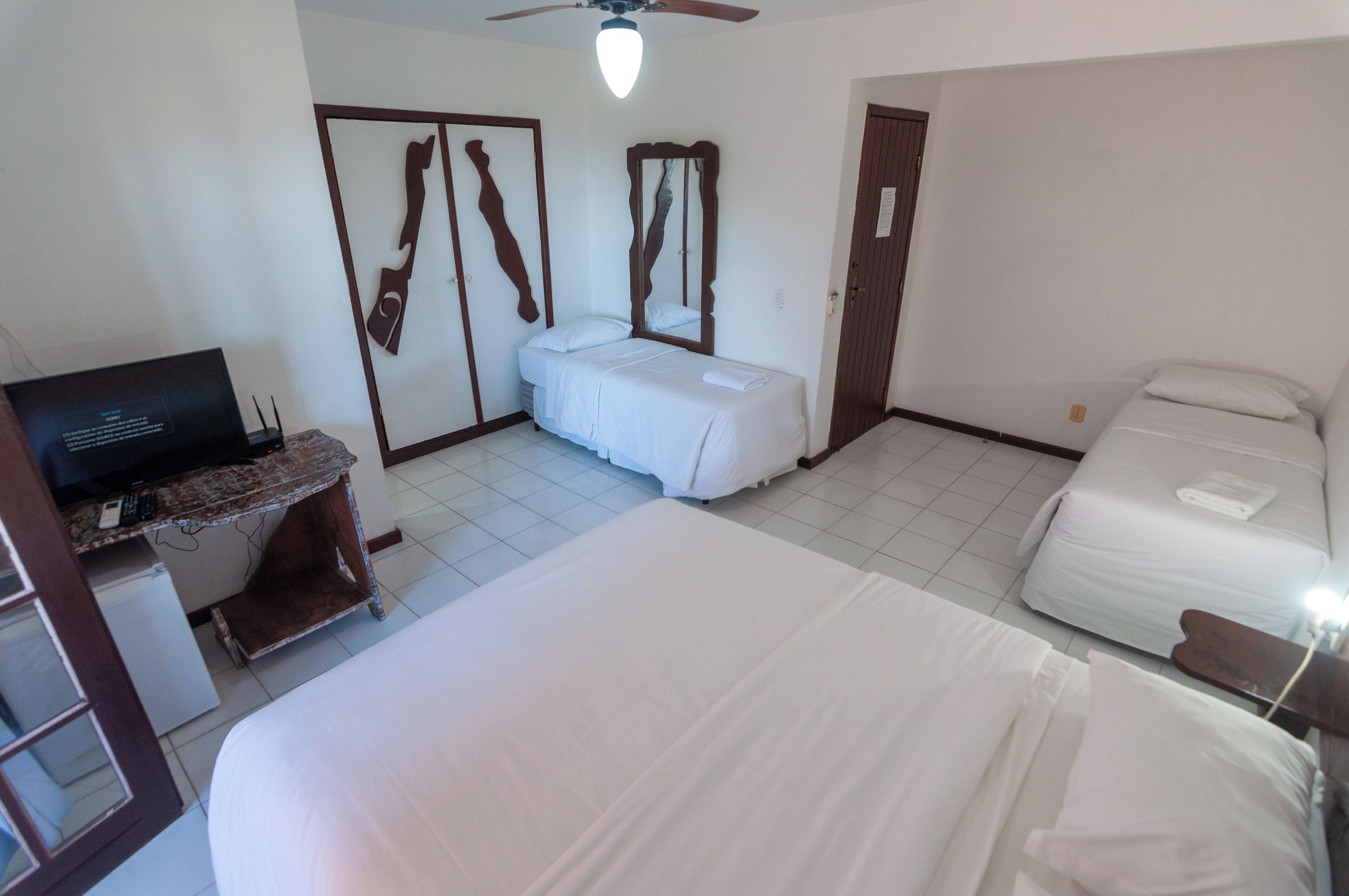 Een hotelkamer met een groot bed, een bureau met een computer, een kledingkast en een spiegel.