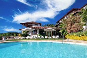 A pool area with lounge chairs and umbrellas, a large house with a tiled roof, and lush greenery. - Arambaré Buzios Hotel (Búzios)