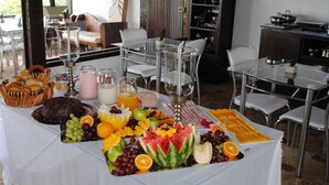 Un buffet de petit-déjeuner proposant une variété de fruits, de jus et de viennoiseries, disposé sur une table dans un espace de restauration moderne, agrémenté de meubles en verre.