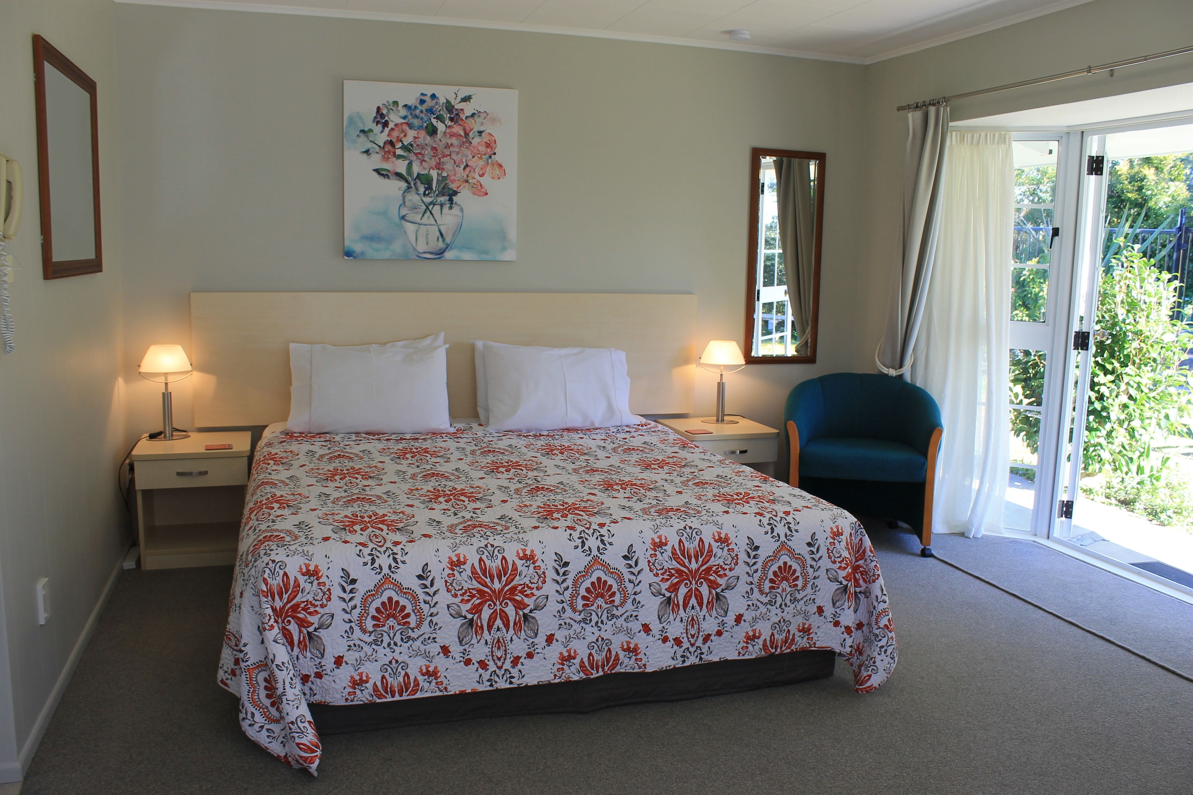 Habitación de hotel con cama, dos lámparas de noche, una silla, un cuadro y una ventana con cortinas.