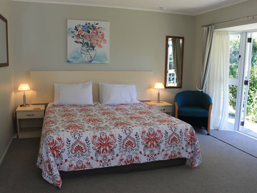 Habitación de hotel con cama, dos lámparas de noche, una silla, un cuadro y una ventana con cortinas.