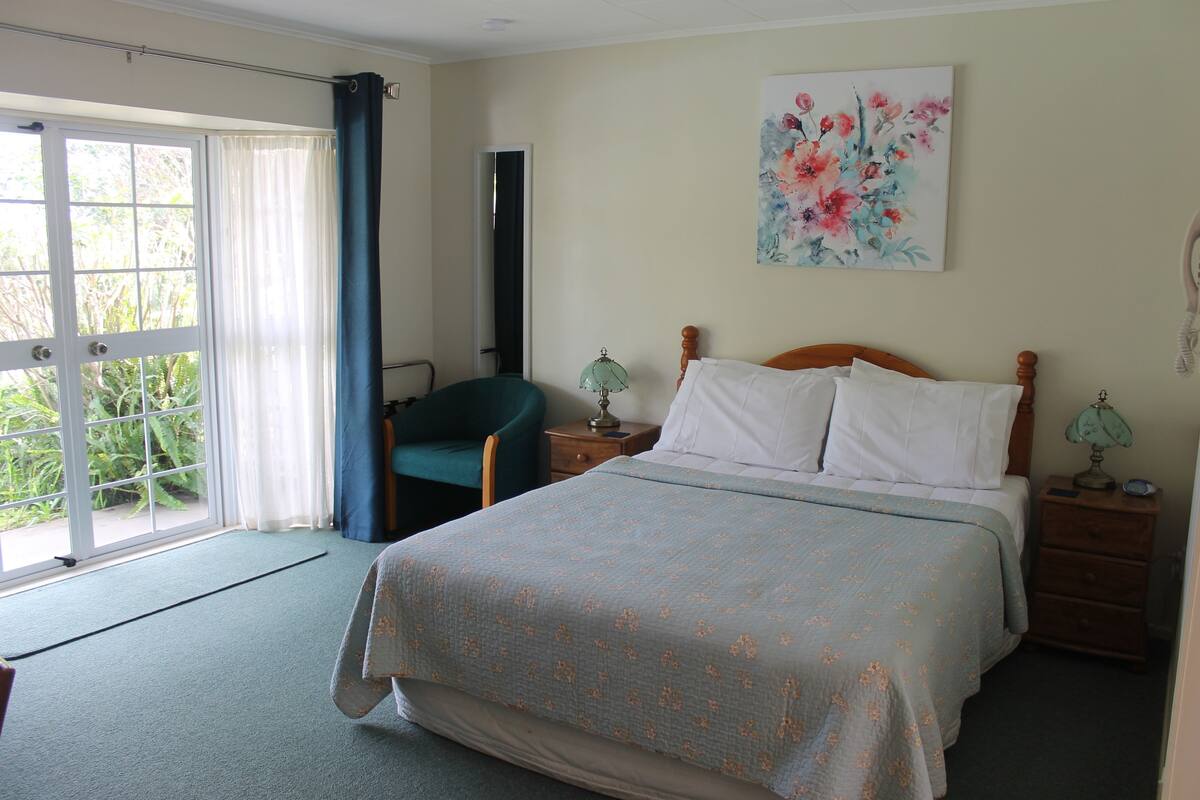 A bedroom with a bed, a chair, a nightstand, a lamp, and a painting on the wall.