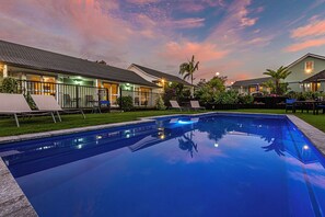 A swimming pool with lounge chairs and a well-lit outdoor area at dusk. - Ash Grove Boutique Motel (Haruru)