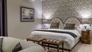 A bedroom with a large bed, two bedside tables with lamps, a framed picture on the wall, and a patterned wallpaper.