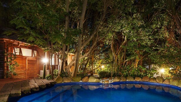 A wooden cabin with a swimming pool surrounded by trees and a stone wall.