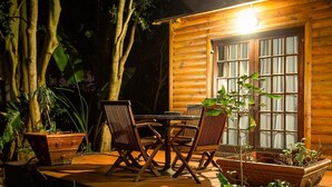 A wooden cabin with a dining table and chairs, surrounded by potted plants and trees.