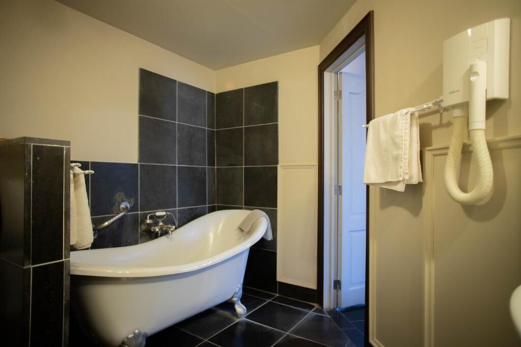 A bathroom with a freestanding bathtub, a towel rack with towels, and a hand dryer on the wall.