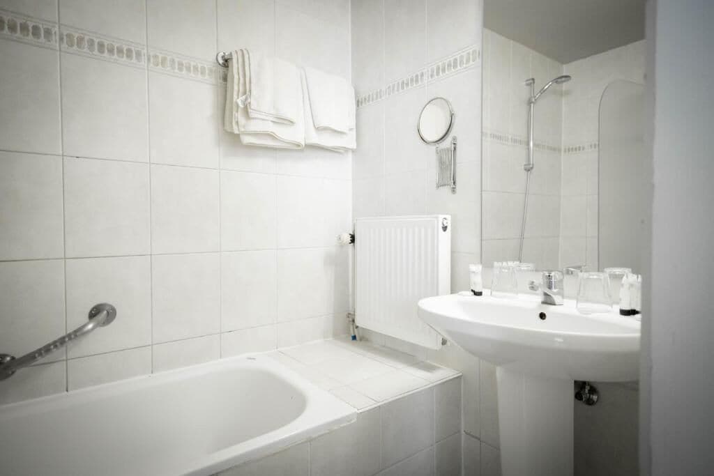 Een badkamer met een bad, een wastafel, een spiegel en een handdoekhouder.