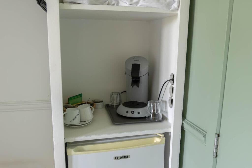A kitchenette with a coffee maker, a small refrigerator, and a glass on the counter.
