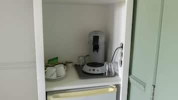 A kitchenette with a coffee maker, a small refrigerator, and a glass on the counter.