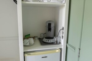 Una kitchenette con cafetera, un refrigerador pequeño y un vaso sobre la encimera.