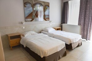 Habitación de hotel con dos camas, un cuadro en la pared, una ventana con cortinas y un radiador.
