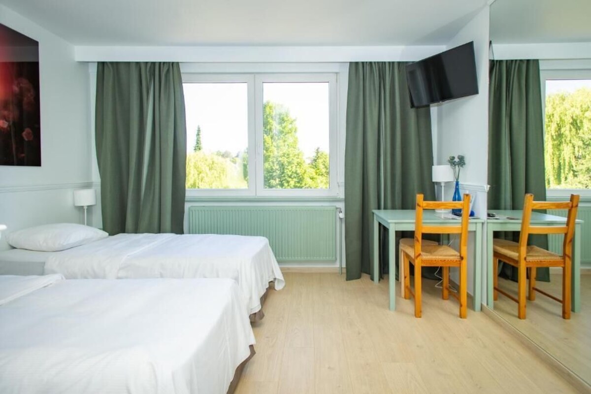 Een hotelkamer met twee bedden, een bureau, een stoel, een televisie en een raam met gordijnen.