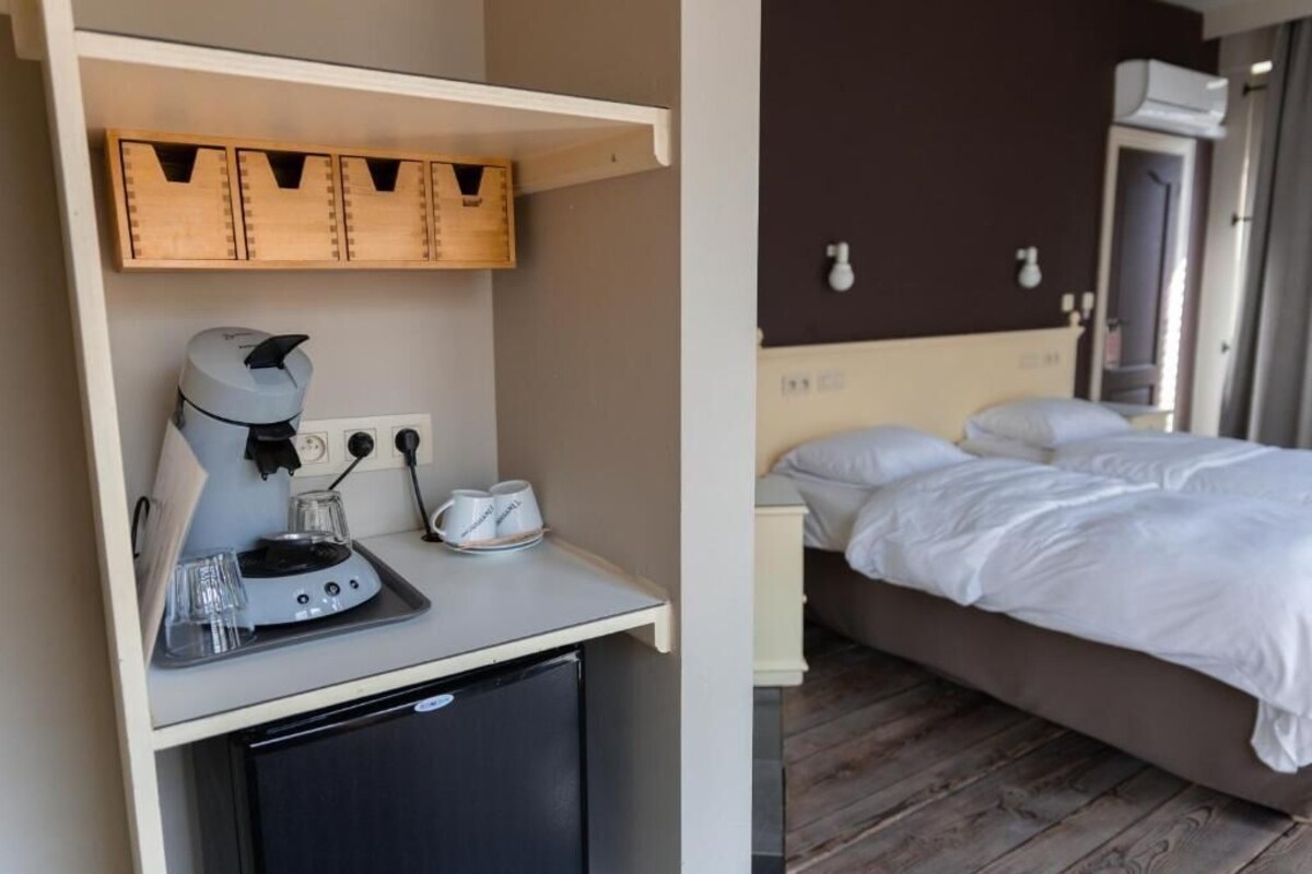Een compacte kamer met een bed, een kitchenette met een koffieapparaat en een houten plank boven het aanrecht.