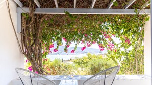 Une terrasse avec deux chaises blanches à armature métallique, une petite table et deux verres à vin.