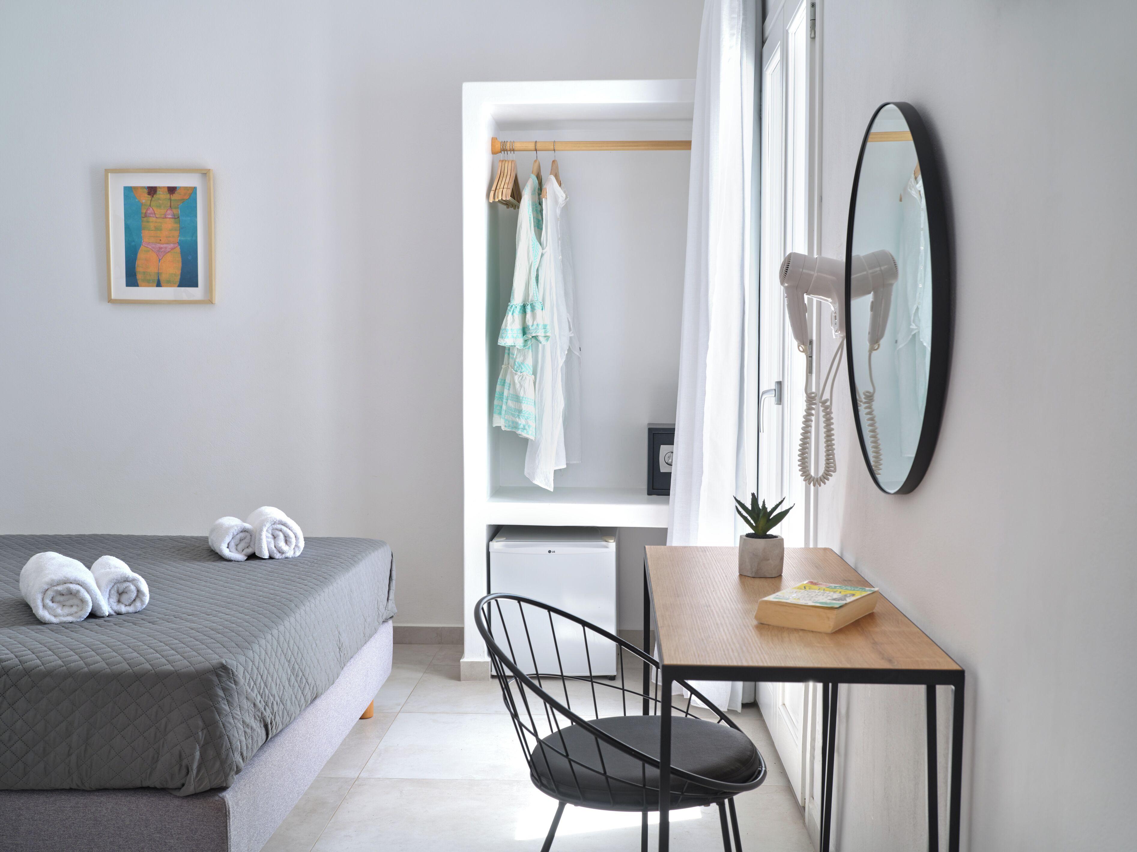 A hotel room with a bed, a desk with a chair, a mirror, and a hanging phone.