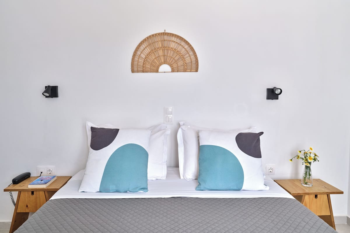 A neatly made bed with two pillows, a bedside table with a book and a phone, and a wall-mounted light fixture.