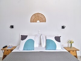 A neatly made bed with two pillows, a bedside table with a book and a phone, and a wall-mounted light fixture.