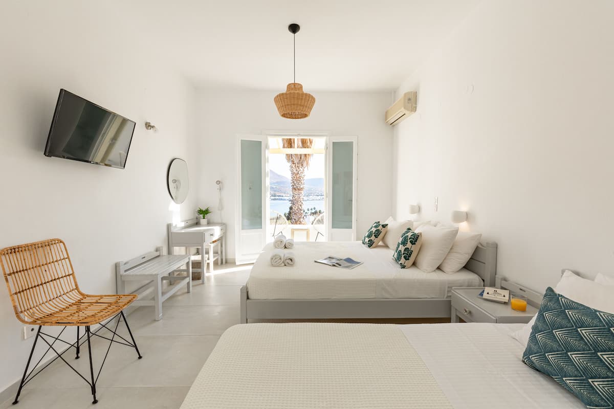 A modern hotel room with a bed, bedside tables, a chair, a TV, and a view of the outdoors.