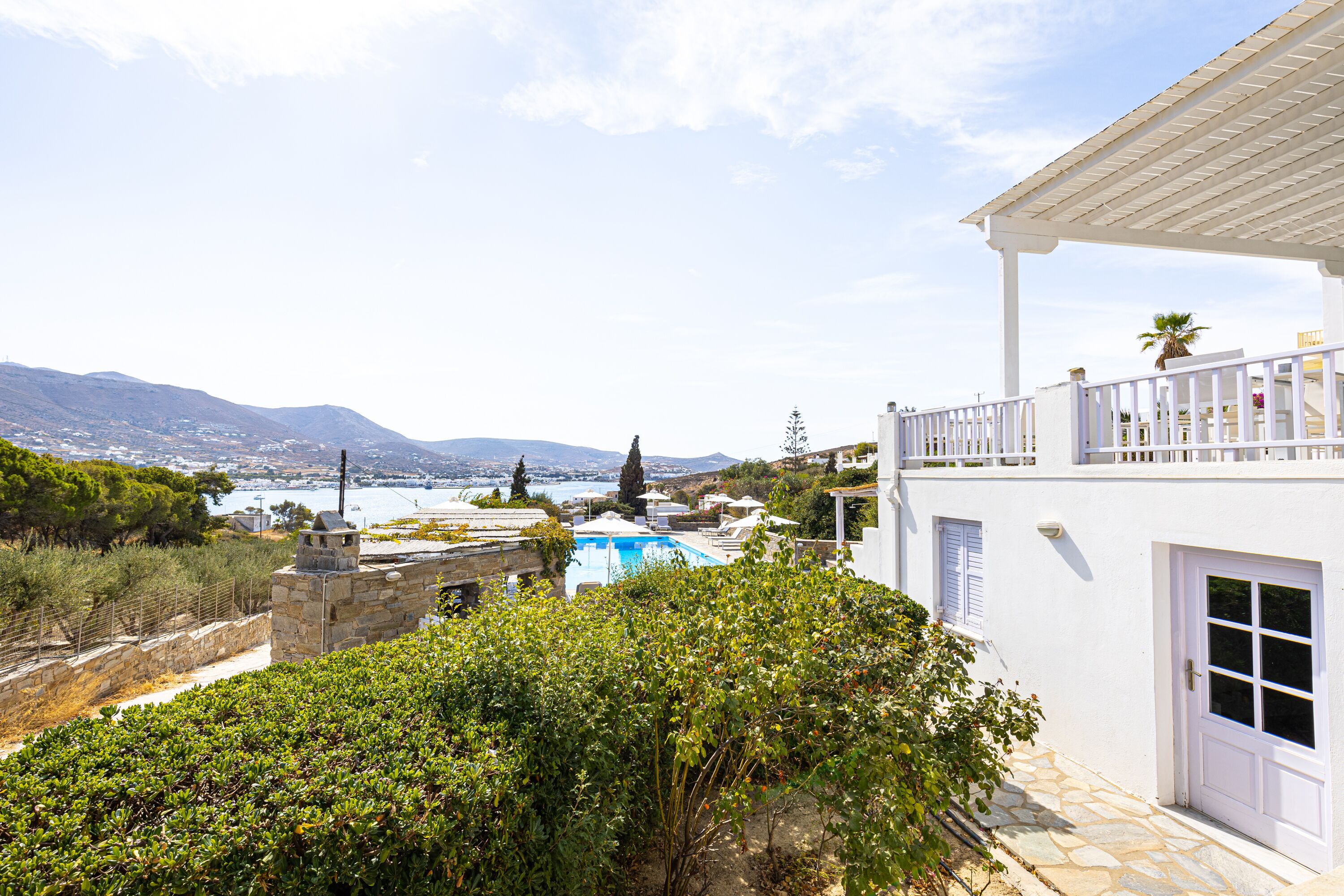 A white building with a pool, stone walls, and a view of the sea and mountains.