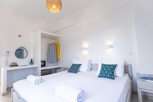 A modern hotel room with a large bed, a bedside table, a desk with a chair, a wardrobe, and a mirror.