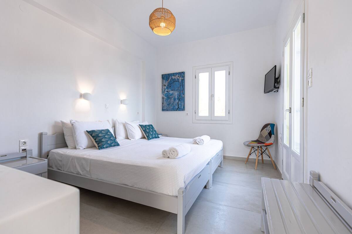 A modern bedroom with a bed, bedside tables, a chair, a TV, and a window.