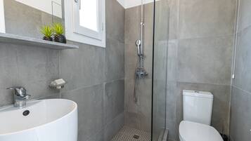 Een moderne badkamer met een vrijstaand bad, een douche met glazen wanden en een toilet.