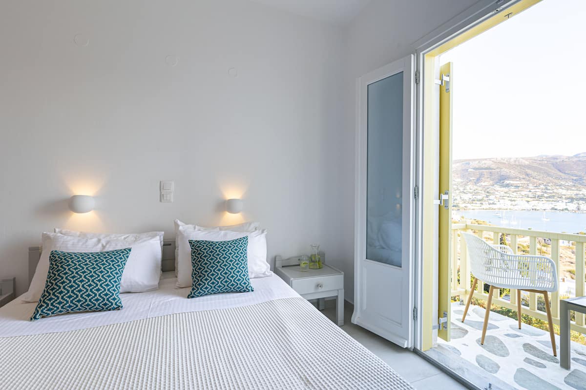 A bedroom with a bed, two bedside lamps, a nightstand, and a view of a balcony with a chair.
