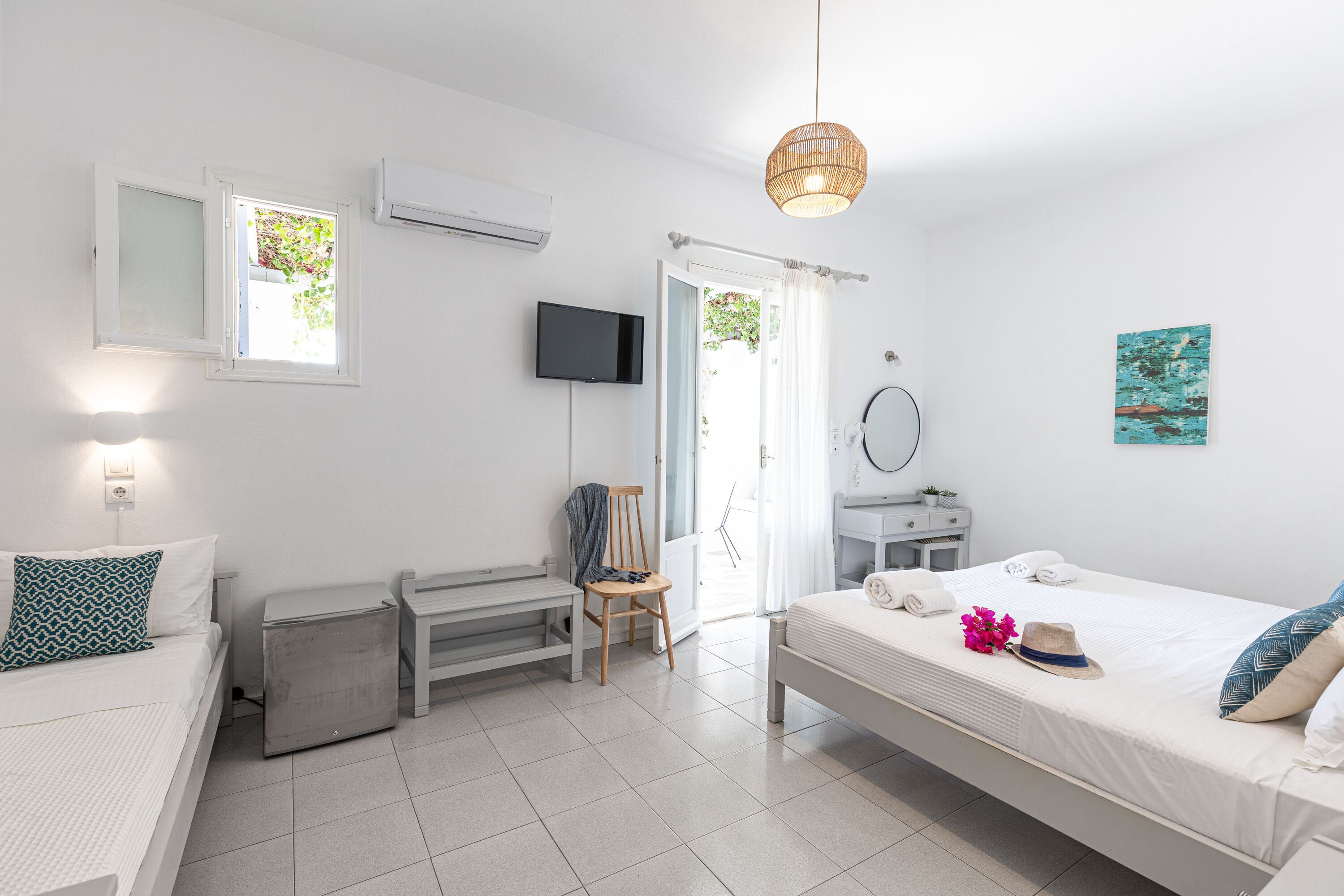 A modern, well-lit bedroom with a bed, a chair, a desk, a television, and a door leading to an outdoor area.